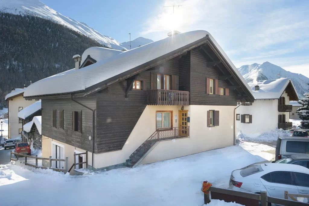 Chalet alpino innevato con montagna sullo sfondo.