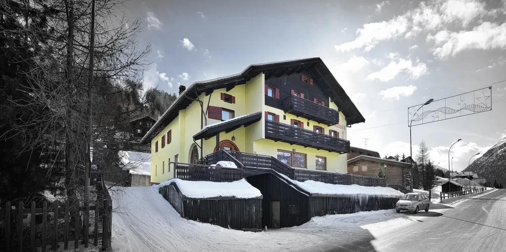Edificio giallo alpino con balconi in legno, circondato da neve e montagne.