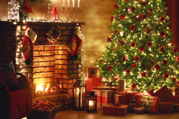 Camino decorato con calze natalizie e albero di Natale illuminato vicino a regali.