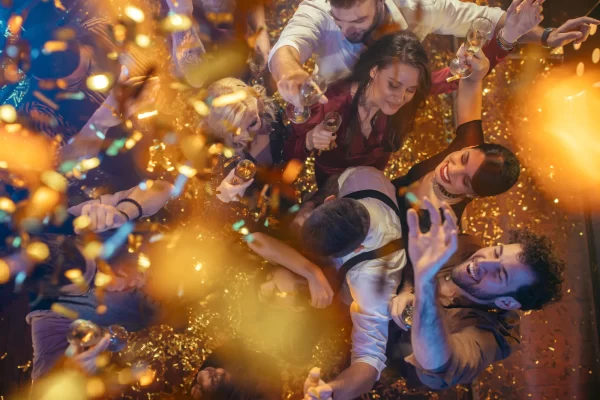 Persone che festeggiano in una discoteca, circondate da luci scintillanti e coriandoli.