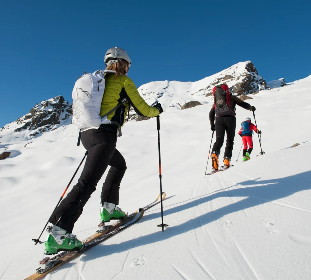 Persone che praticano sci alpinismo su una montagna innevata sotto un cielo limpido.